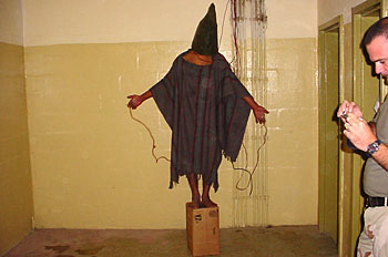 ▲アブグレイブ刑務所での米軍によるイラク人拘留者に対する虐待の様子。この人物は両手と性器にワイヤーをつけられ、箱から降りようとすると電気を流されたという（写真：Wikipedia）