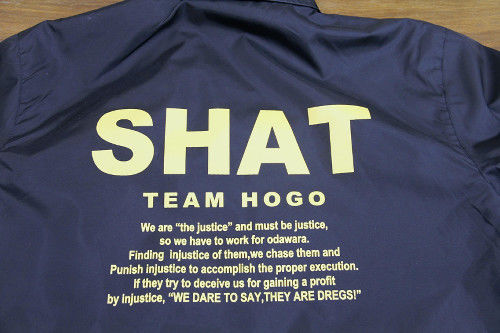 ▲小田原市役所によれば、背中のロゴの「SHAT」は、生活（S）保護（H）悪撲滅（A）チーム（T）の略だという。なお英語のSHATはSHIT（クソ、クズ）の過去・過去分詞形